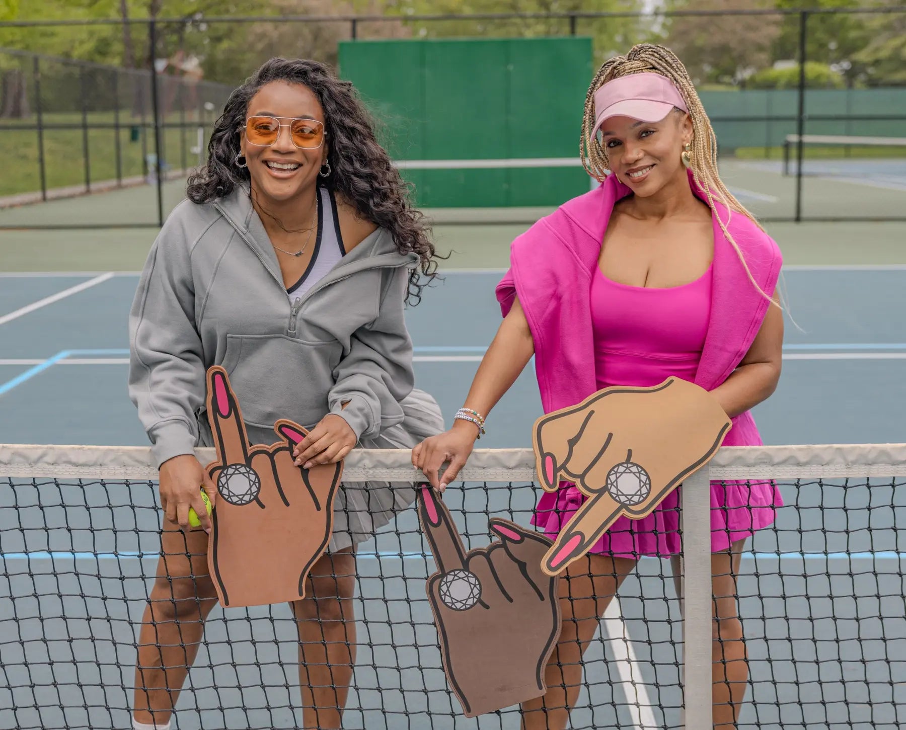Friends celebrating with all-shades Brown Skin Bride foam fingers on a tennis court